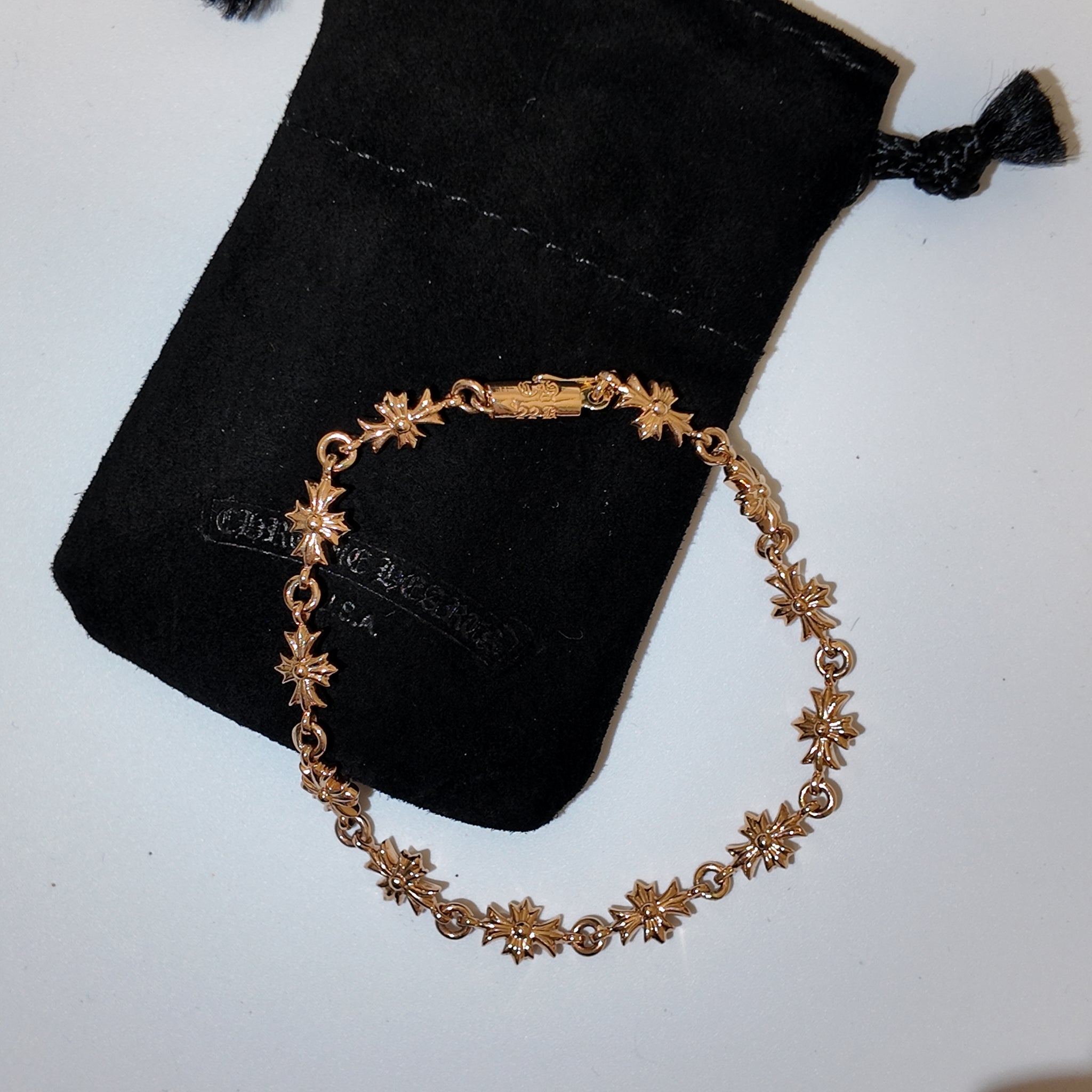A gold-toned bracelet with repeating flower motifs, displayed on a black velvet jewelry pouch against a light gray background.