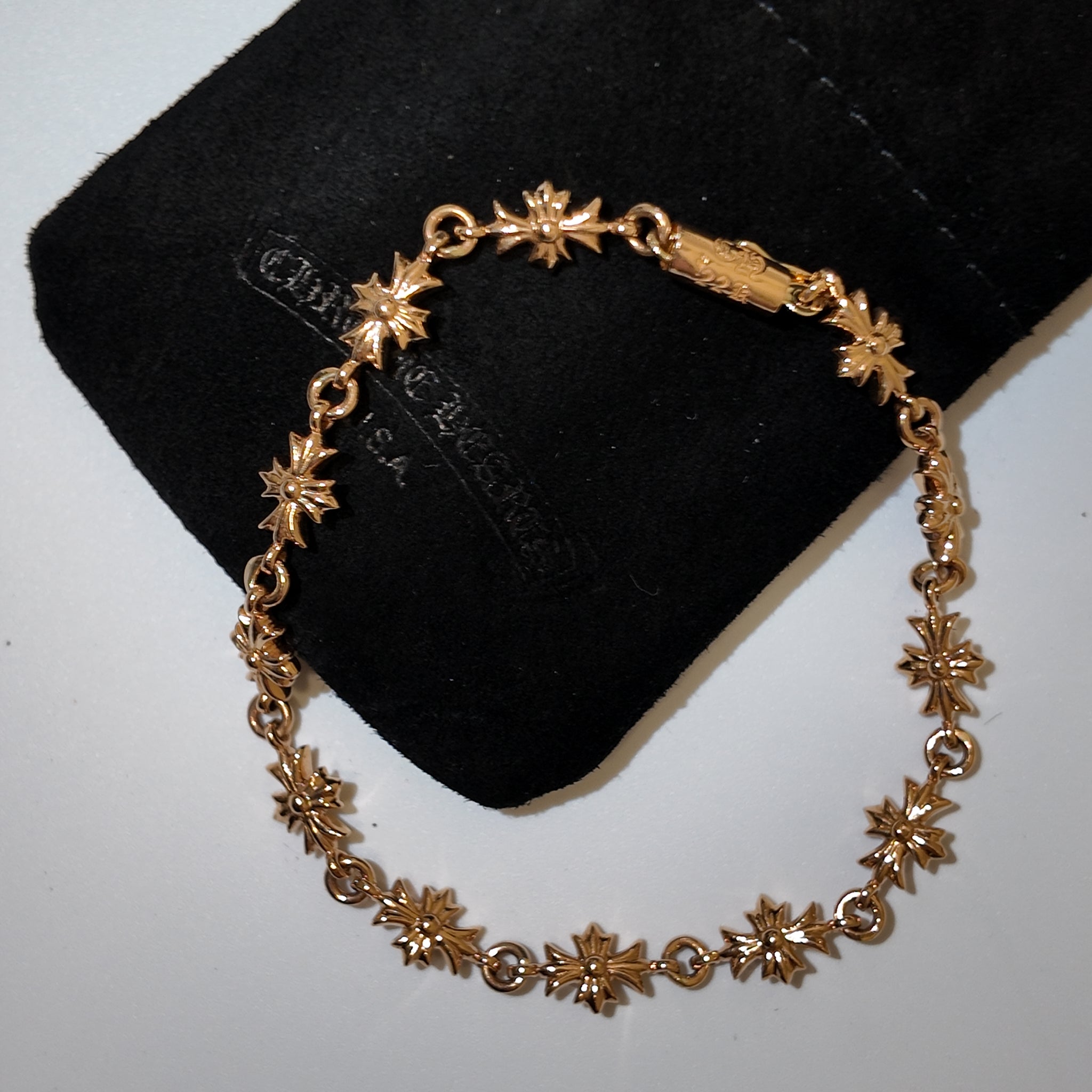 A gold-toned link bracelet with repeating starburst motifs, displayed on a black velvet jewelry pouch against a light gray background.