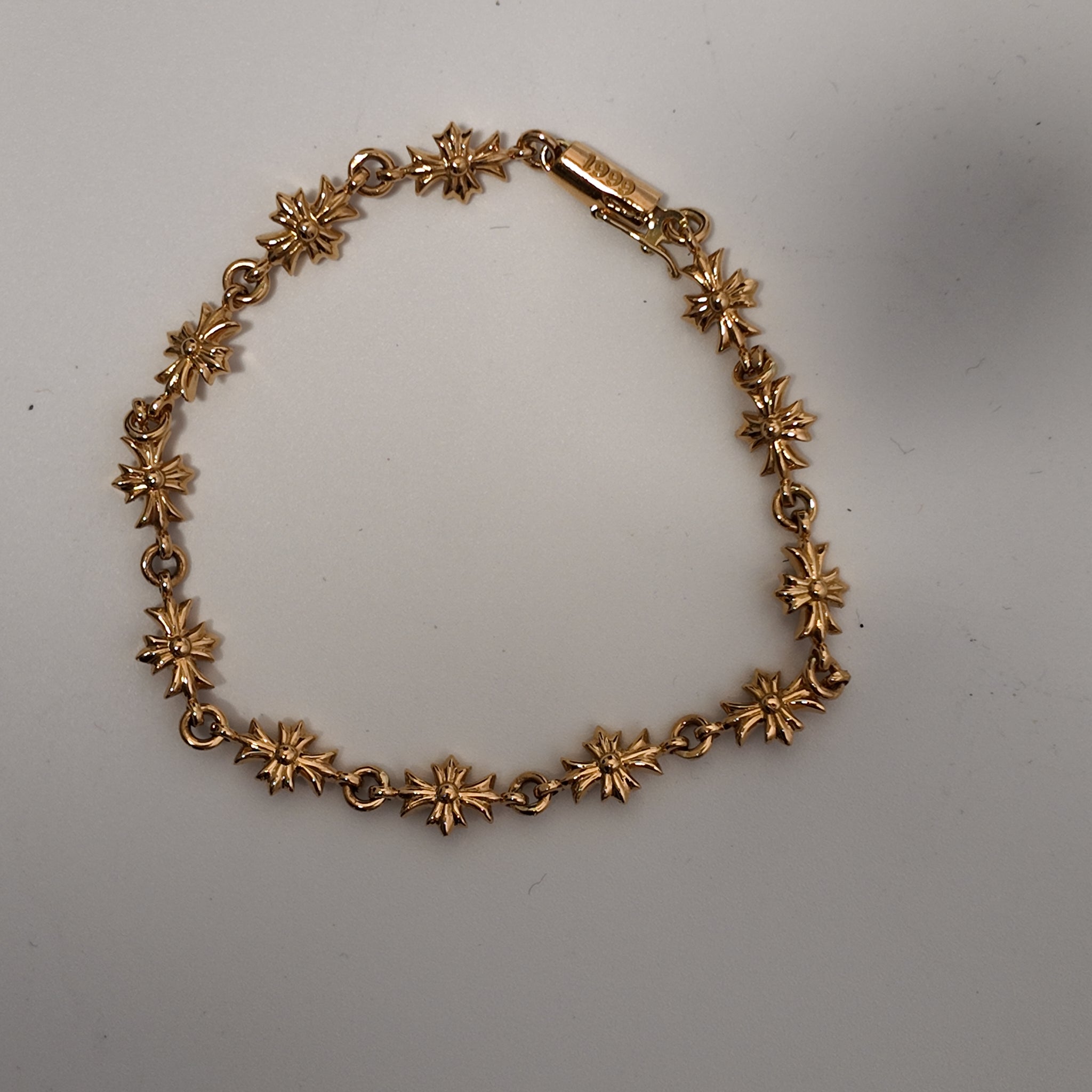 A vintage gold-tone chain bracelet featuring repeating starburst or flower-like links, displayed on a plain light gray surface.