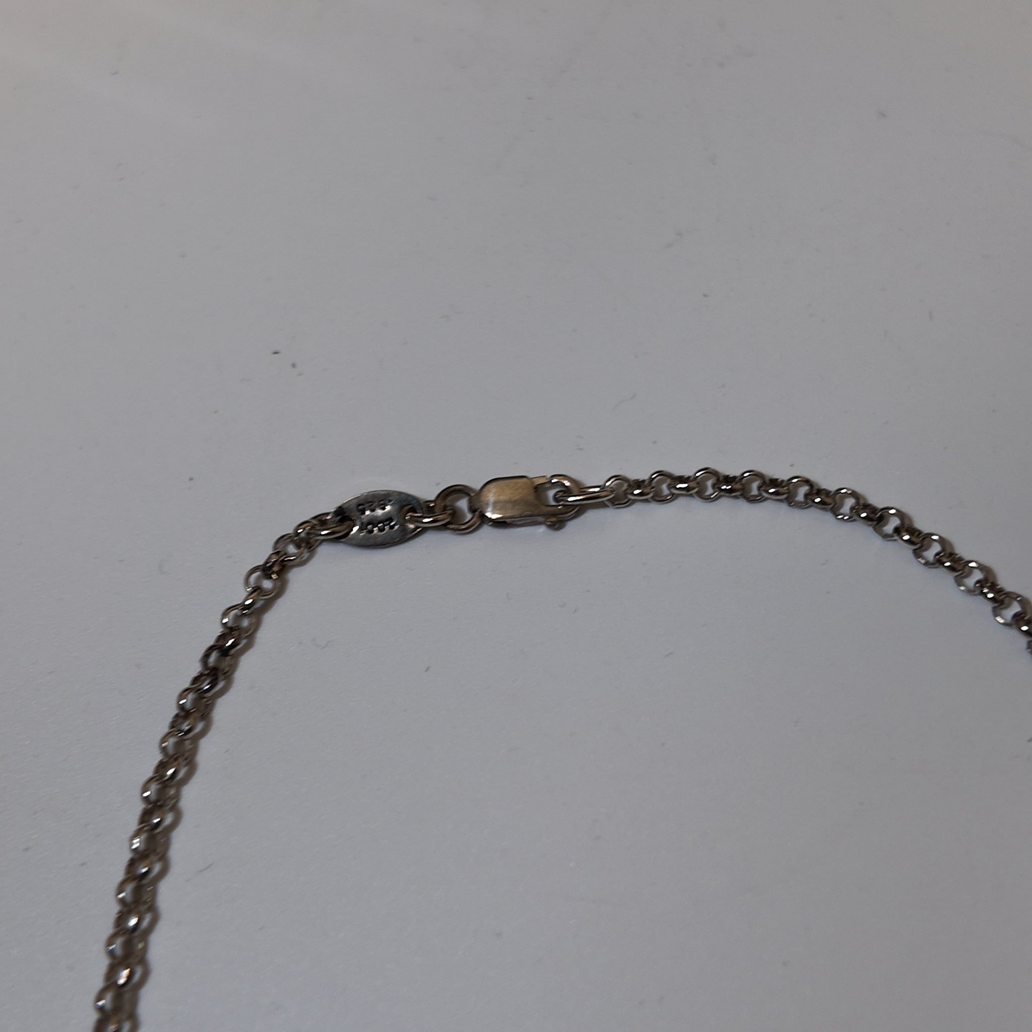 Close-up of a silver-toned metal chain necklace with a lobster clasp on a plain light gray background.