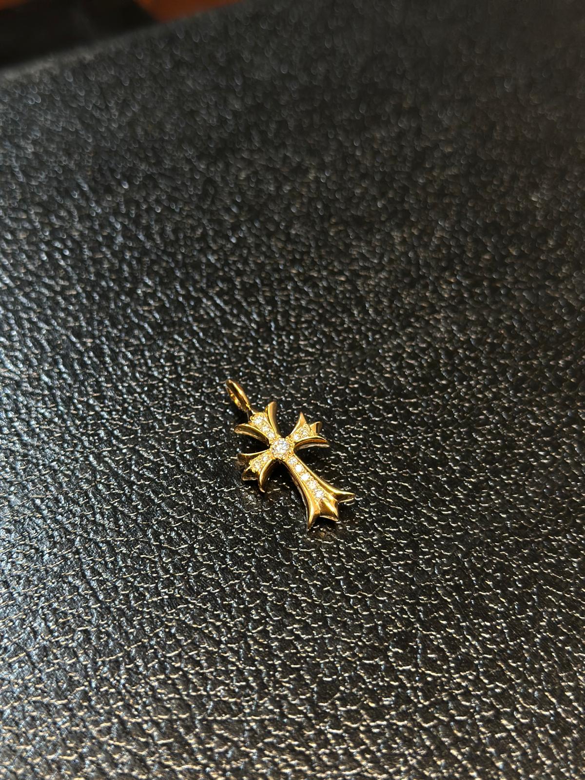 A small gold cross pendant with a clear gemstone at its center, resting on a textured black surface.