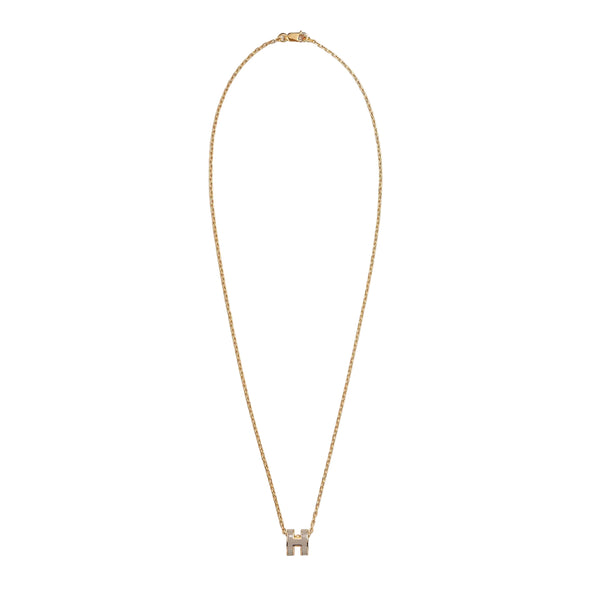 A delicate gold chain necklace with a small bow-shaped pendant set with clear stones, displayed against a solid light beige background.