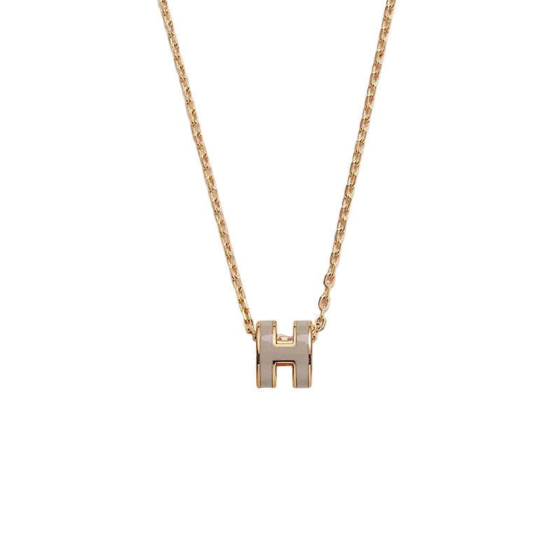 Gold necklace with a 'H' pendant on a light gray background