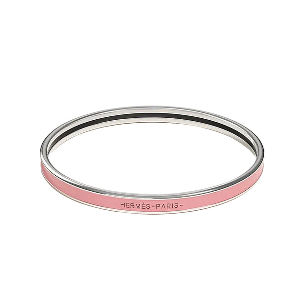 A slim silver-toned bangle bracelet with a light pink enamel band and the text 'HERMÈS-PARIS-' printed in black on the front, set against a clean off-white background.